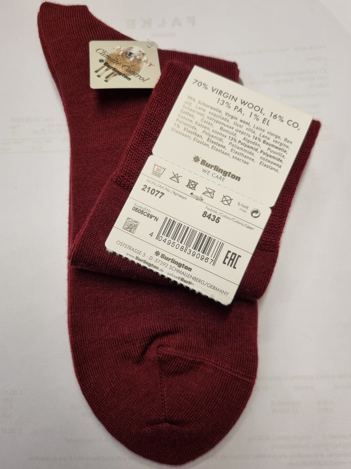 A pair of burgundy knit socks with white paper tags attached, laid flat on a white surface.