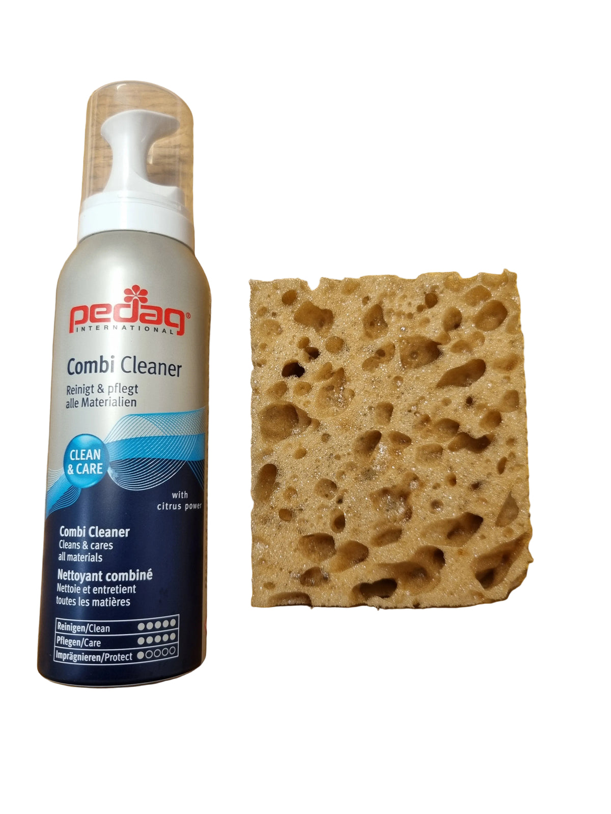A can of Peajag Comb Cleaner foam cleaner placed next to a brown porous cleaning sponge on a wooden tabletop.