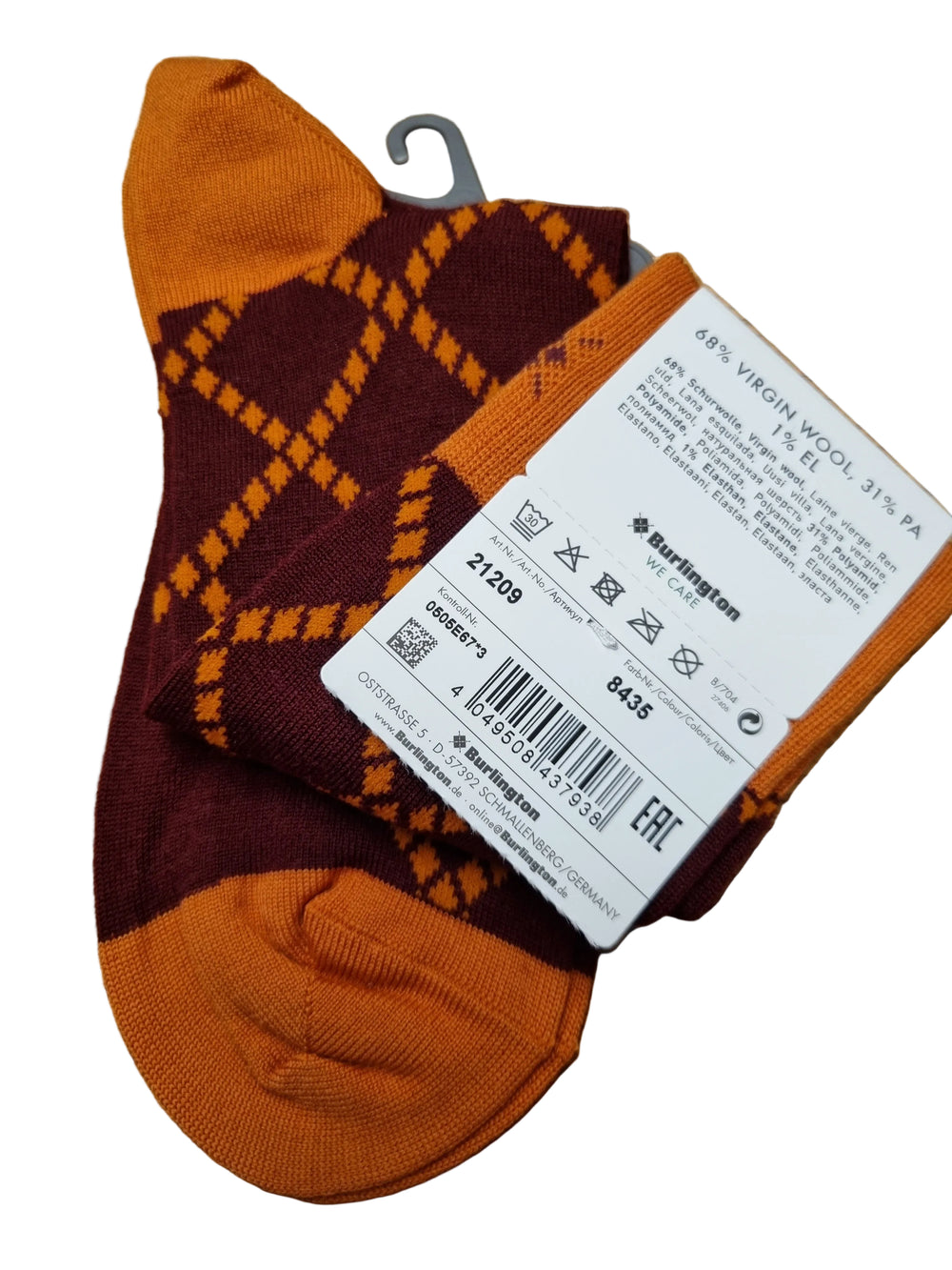 A pair of Burlington argyle socks in orange and burgundy, with a white product tag attached, laid flat on a wooden surface.