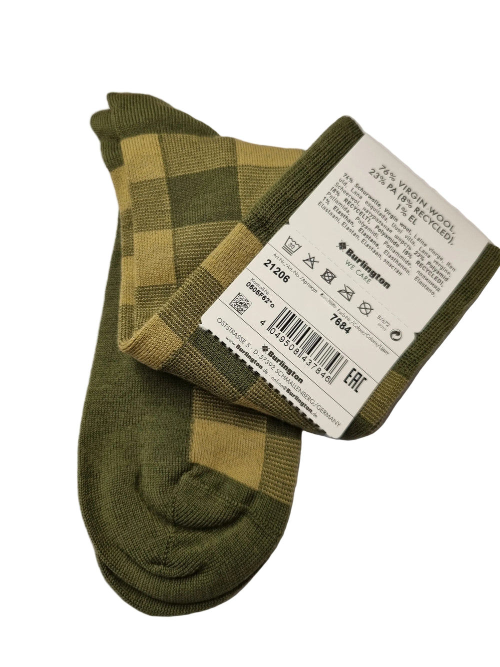 A pair of green and beige buffalo plaid socks with a white paper tag attached, resting on white paper over a wooden desk.