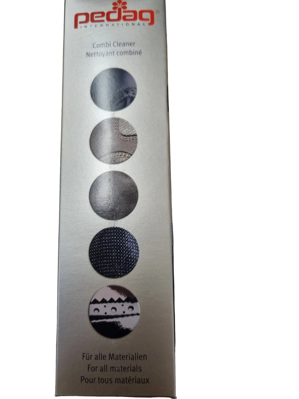 A tall rectangular Pedag Combi Cleaner box standing on a wooden tabletop. The packaging is metallic silver with red Pedag branding at the top and five circular material-use icons printed vertically in dark gray and black.