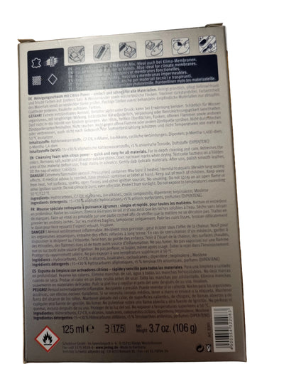 The back of a rectangular product box photographed from above on a wooden tabletop. The box has a dark gray to black label with white text, icons, and a barcode, and a small red hazard symbol near the bottom left.